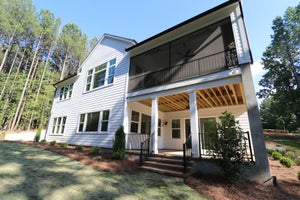 Two-story white home with covered back porch, screened upper balcony, and wooded backyard setting