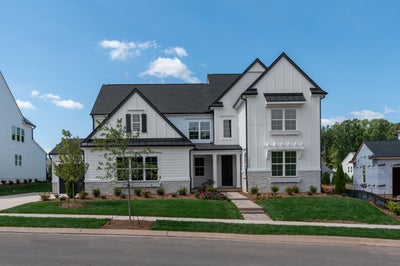 Two-story white farmhouse-style home with stone base, dark roof, black shutters, and landscaped front yard