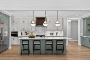 Kitchen with sage green island, four bar stools, white cabinets, marble backsplash, and pendant lights