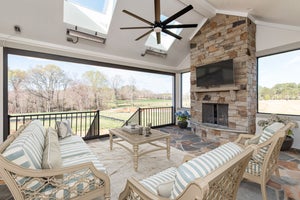 Covered porch with stone fireplace, ceiling fan, skylights, and outdoor seating overlooking a yard