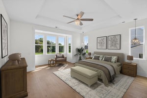 Spacious master bedroom with hardwood floors, bay windows, ceiling fan, and neutral furnishings including a king bed and sitting area.
