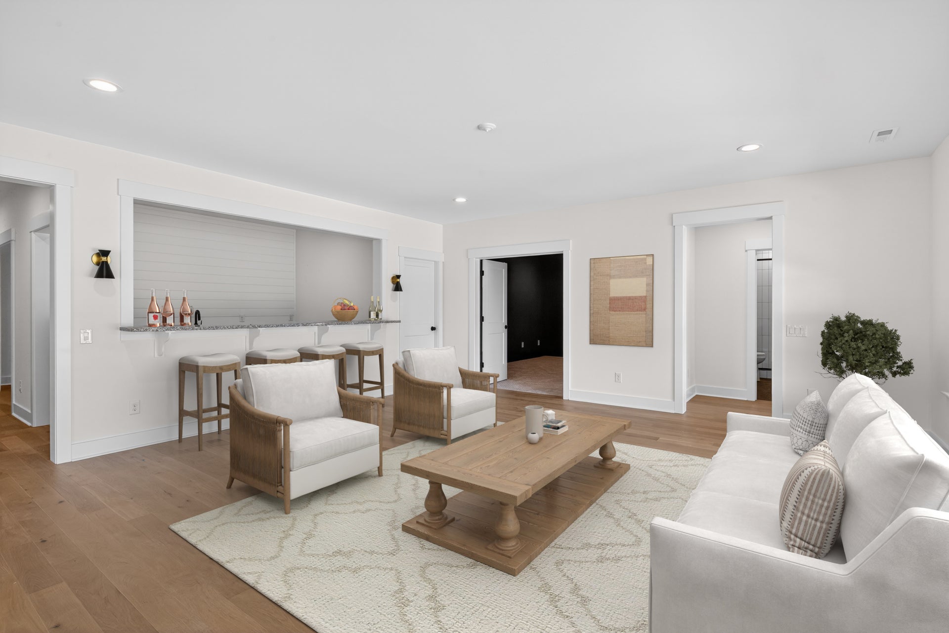Open living room with white seating, wood coffee table, and built-in wet bar with bar stools on hardwood floors