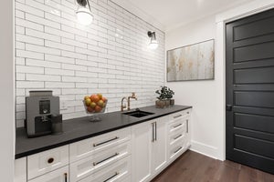 Butler's pantry with white cabinets, black countertop, subway tile backsplash, and gold hardware