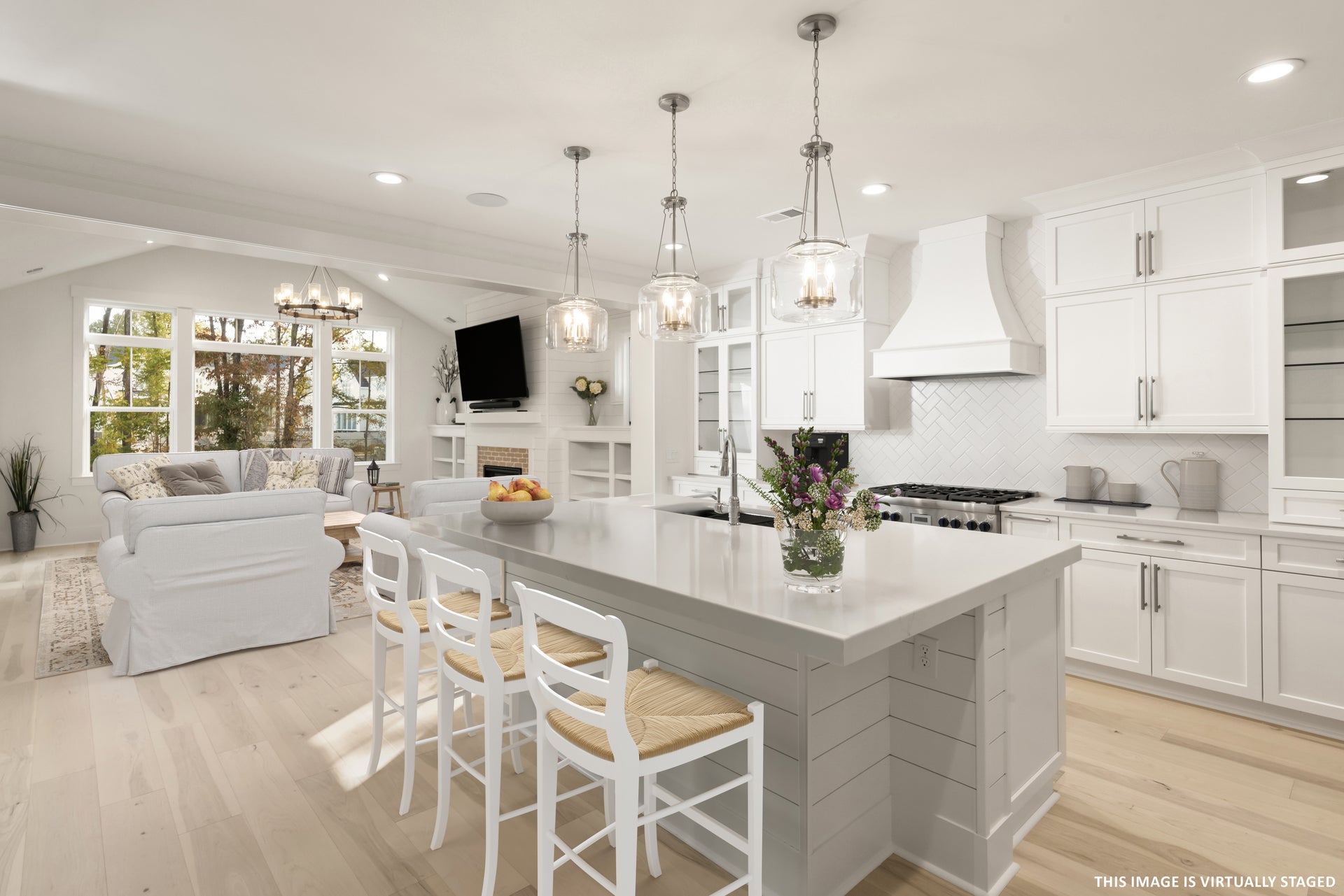 Open-concept kitchen with white cabinets, large island with seating, and adjoining living room with fireplace