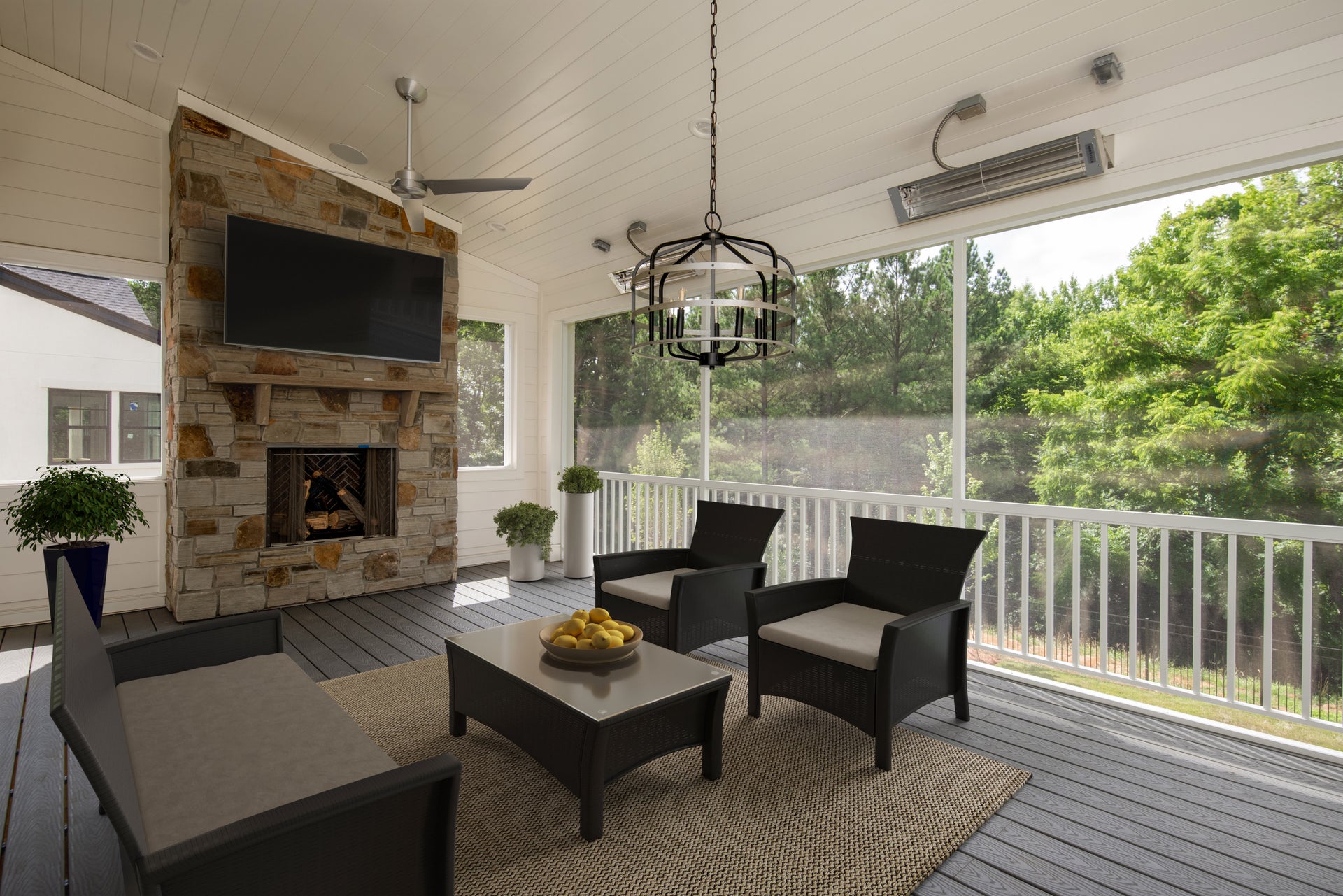 Covered porch with stone fireplace, mounted TV, dark wicker seating, and screened views of trees