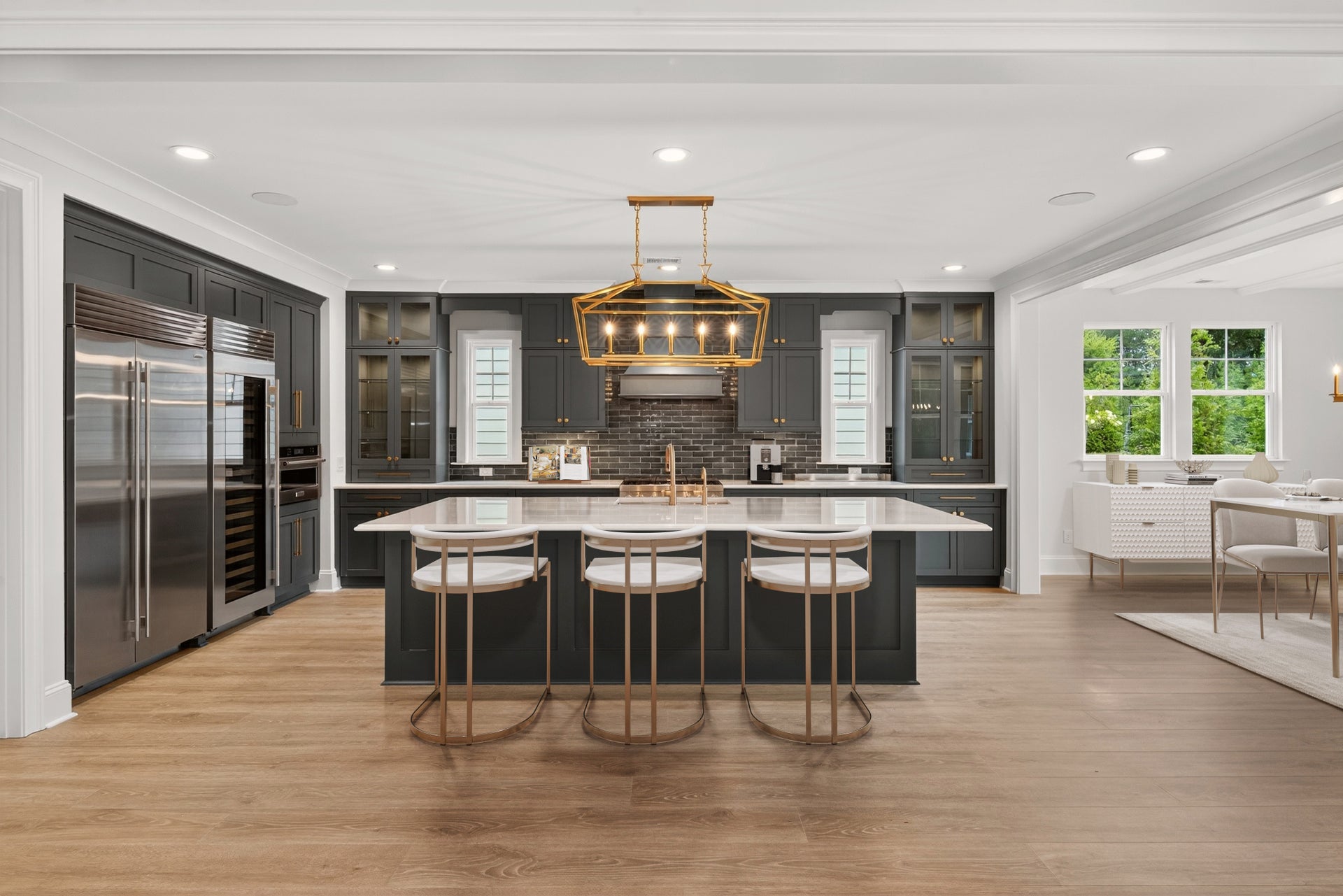 Dark gray kitchen with large island, gold pendant light, and stainless steel appliances on hardwood floors
