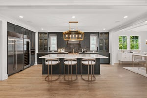 Dark gray kitchen with large island, gold pendant light, and stainless steel appliances on hardwood floors