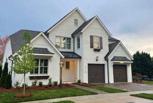 Two-story white brick home with dark shutters, metal roof accents, and two-car garage