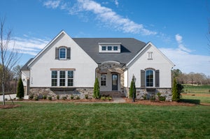 Single-story home with white stucco and stone exterior, arched entry, gray shutters, and manicured front lawn