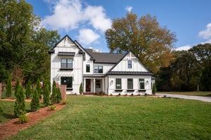 Two-story modern farmhouse with white board-and-batten siding, black metal roof, and covered front porch on a green lawn