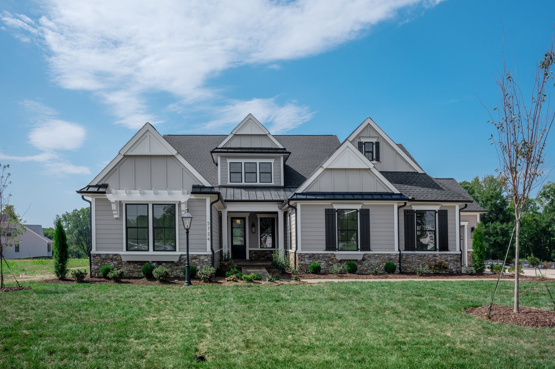Craftsman-style home with gray board-and-batten siding, stone base, covered porch, and front lawn