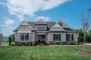 Craftsman-style home with gray board-and-batten siding, stone base, covered porch, and front lawn