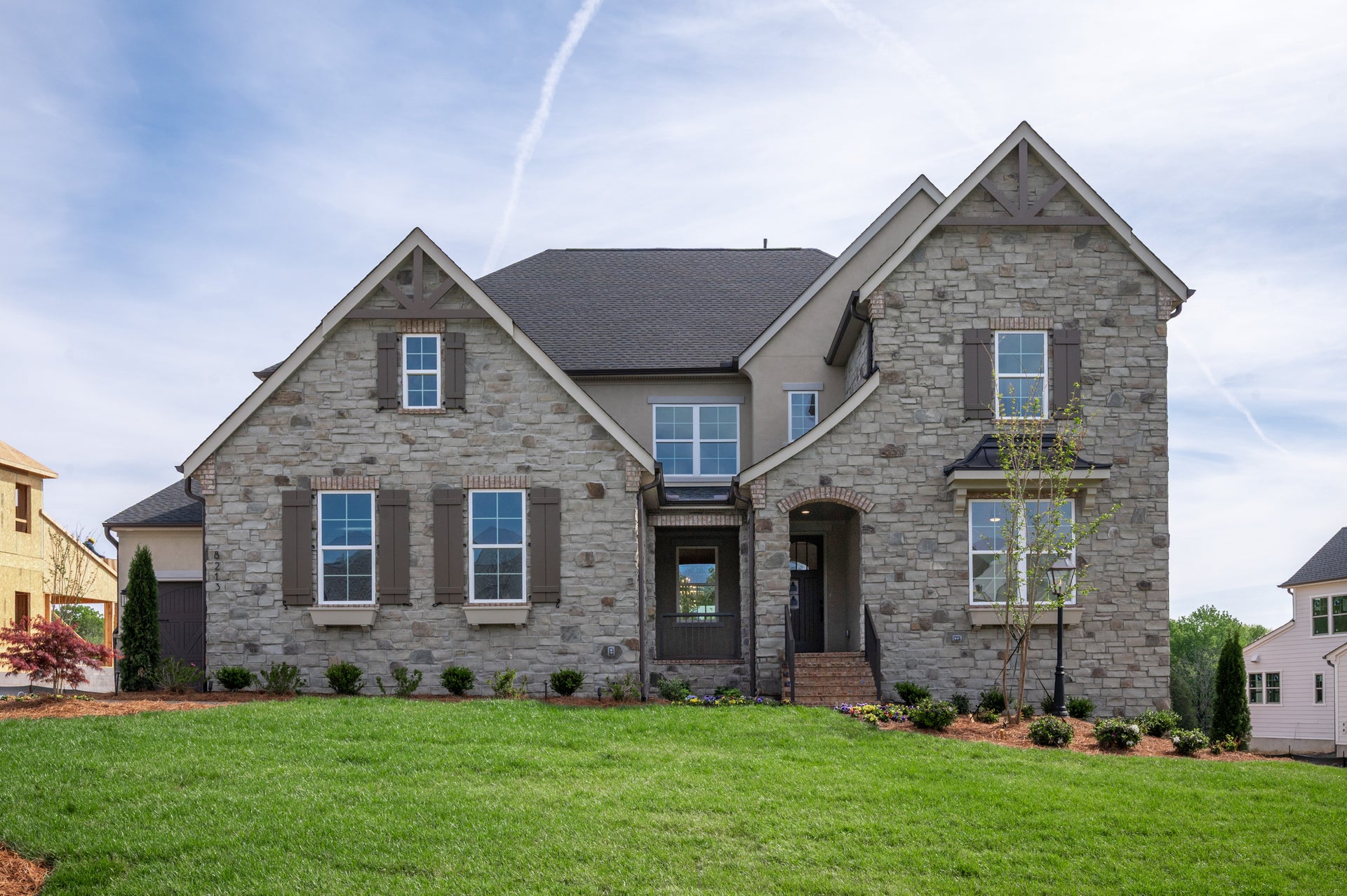 Two-story stone home with dark shutters, arched entry, and manicured front lawn