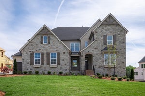 Two-story stone home with dark shutters, arched entry, and manicured front lawn