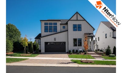Two-story white farmhouse-style home with dark trim, two-car garage, and brick paver driveway