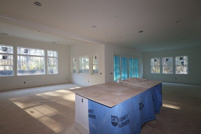 Open-concept home interior under construction with a large kitchen island wrapped in protective covering and multiple windows.