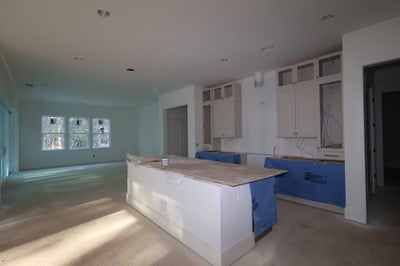 Kitchen under construction with white cabinets, center island, and protected countertops open to living area