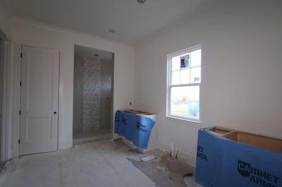 Bedroom under construction with protected cabinets, white walls, and tiled bathroom visible through doorway