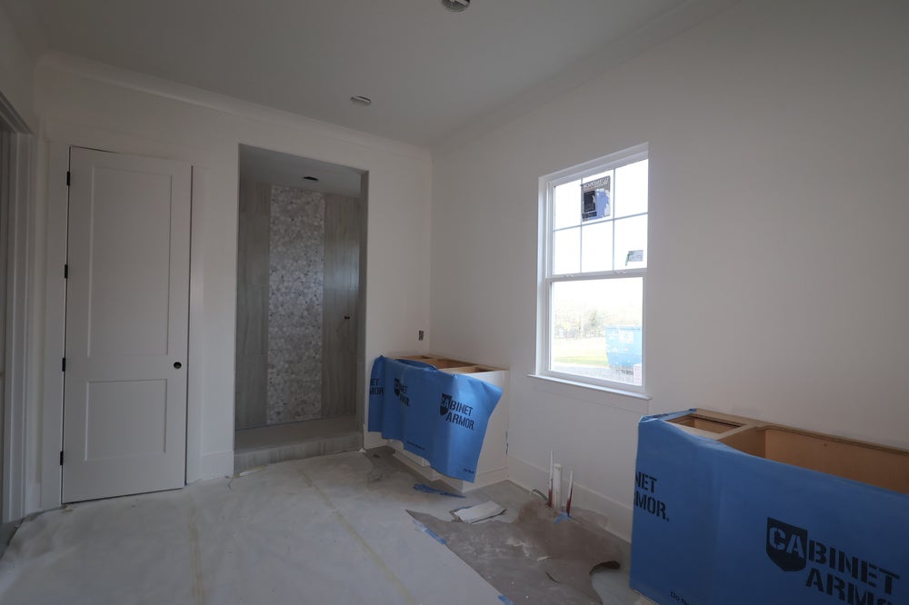 Bedroom under construction with protected cabinets, white walls, and tiled bathroom visible through doorway