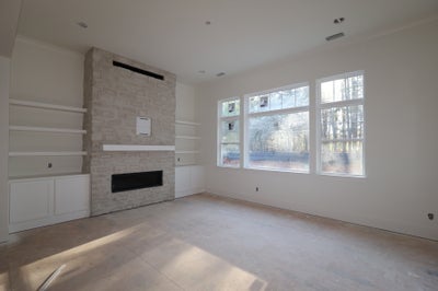 Unfurnished living room with stone fireplace, built-in shelves, and large windows under construction