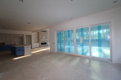 Open-concept living area under construction with large sliding glass doors, fireplace, and built-in shelving visible in background.