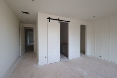 Empty bedroom with white sliding barn door leading to bathroom and hallway beyond