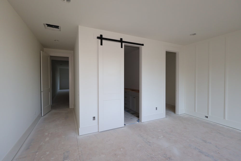 Empty bedroom with white sliding barn door leading to bathroom and hallway beyond