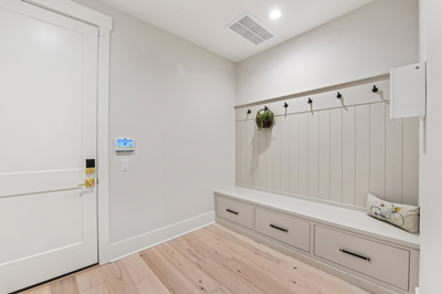 Mudroom with built-in bench, storage drawers, coat hooks, and light wood floors near entry door