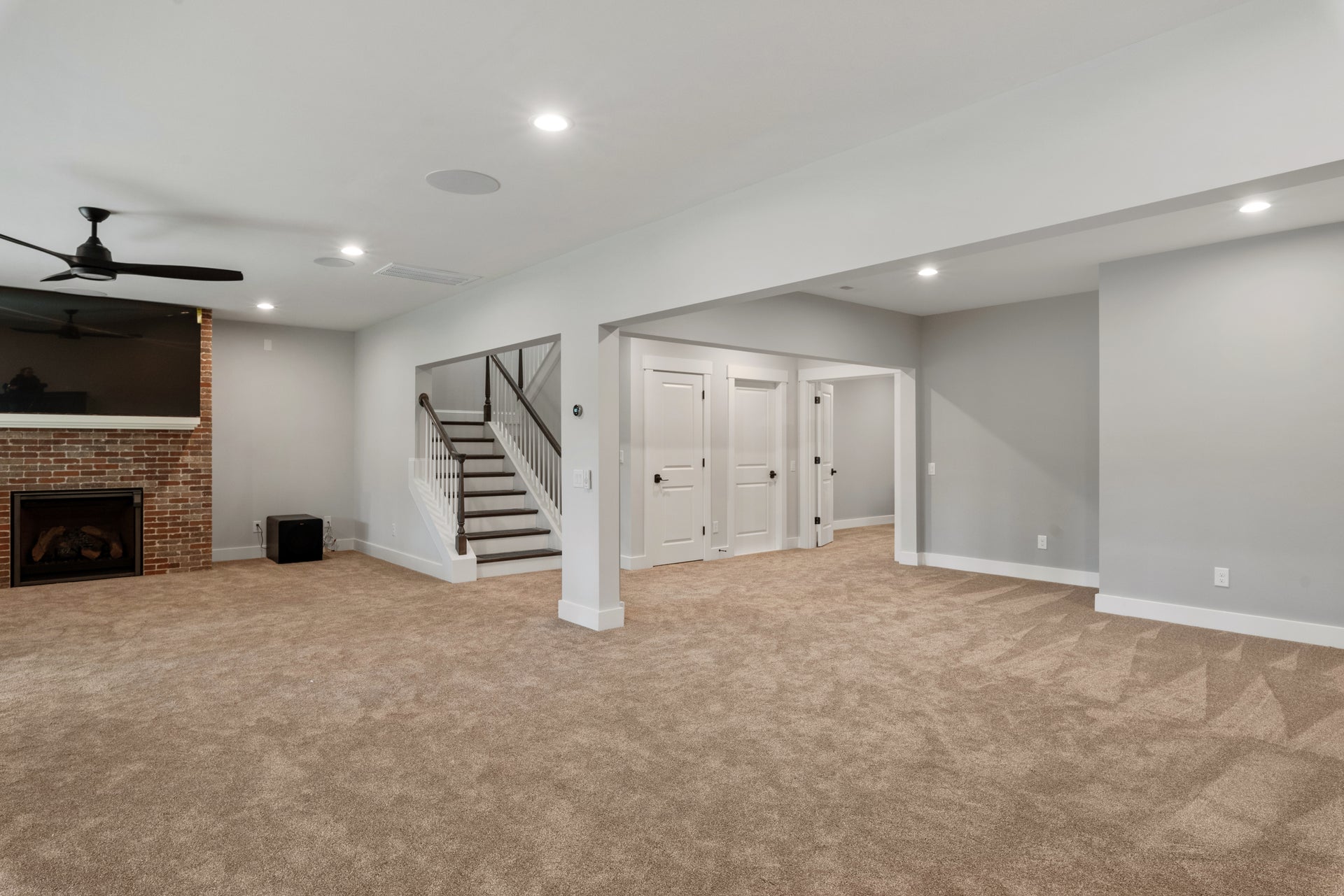 Finished basement with brick fireplace, carpet flooring, ceiling fan, and staircase leading upstairs