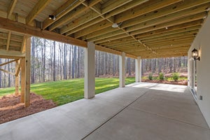 Covered patio with exposed wood beam ceiling, concrete floor, and wooded backyard view