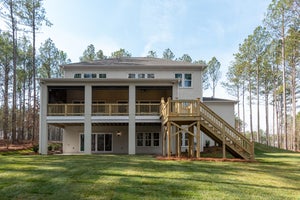 Rear exterior of two-story home with raised screened porch, wooden deck, and staircase surrounded by trees and lawn