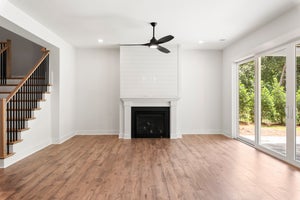 Open living room with shiplap fireplace, hardwood floors, ceiling fan, staircase, and sliding glass doors to patio