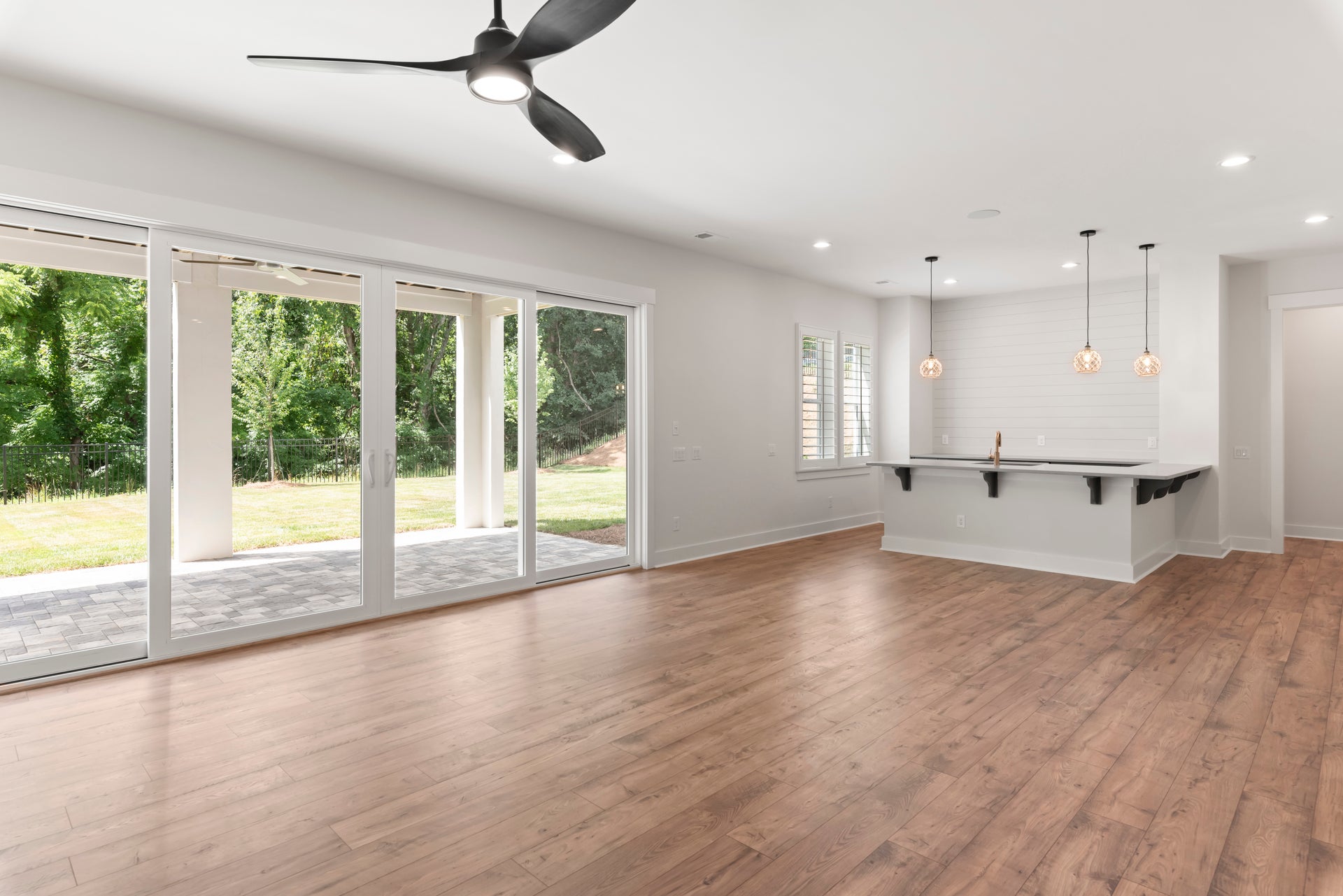 Open living area with hardwood floors, ceiling fan, sliding glass doors, and kitchen bar with pendant lights