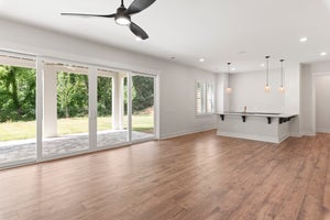 Open living area with hardwood floors, ceiling fan, sliding glass doors, and kitchen bar with pendant lights