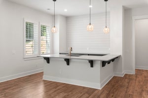 Kitchen island with sink, bar seating, three pendant lights, and shiplap accent wall on hardwood floors