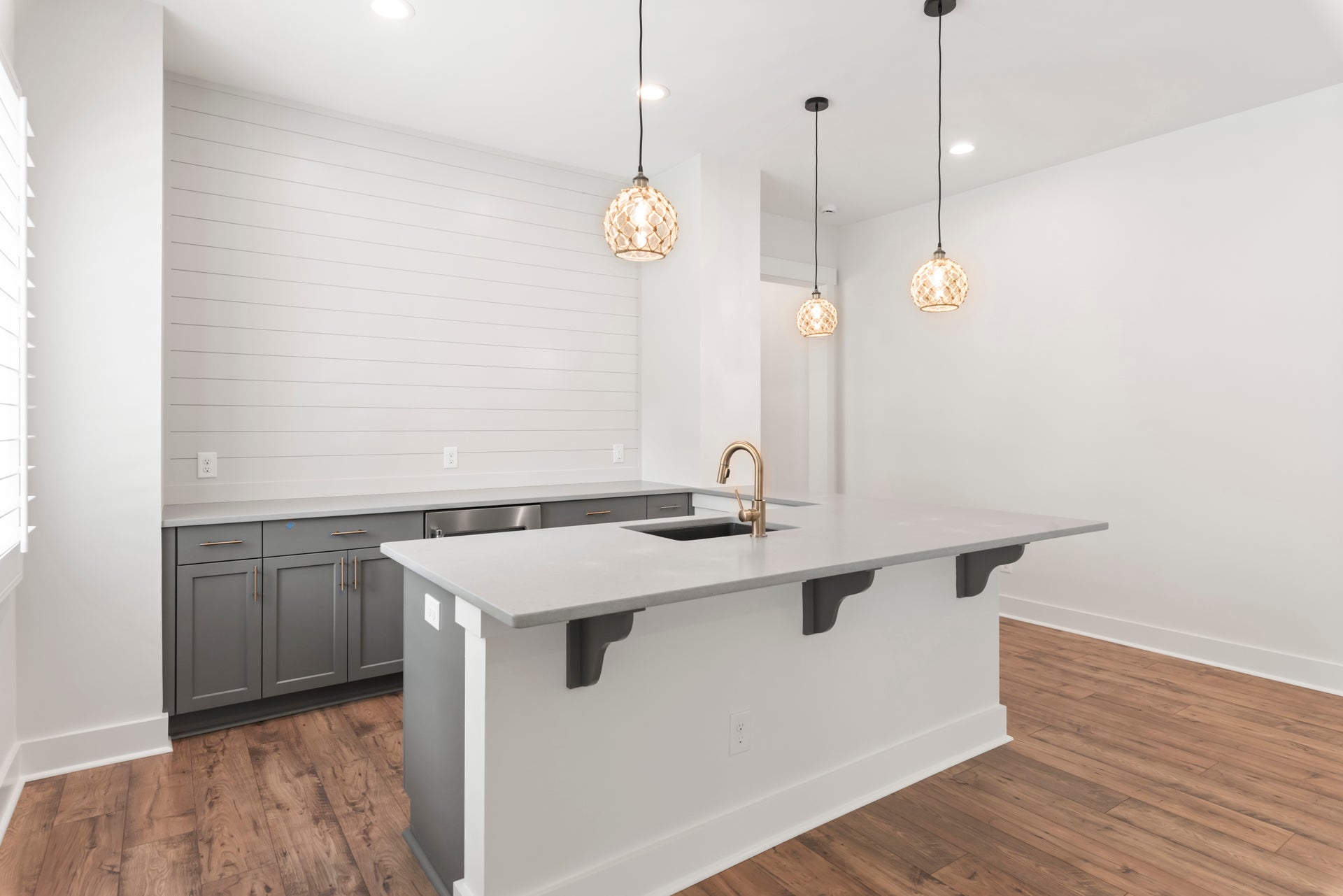 Kitchen island with sink, gray cabinets, shiplap wall, pendant lights, and hardwood floors