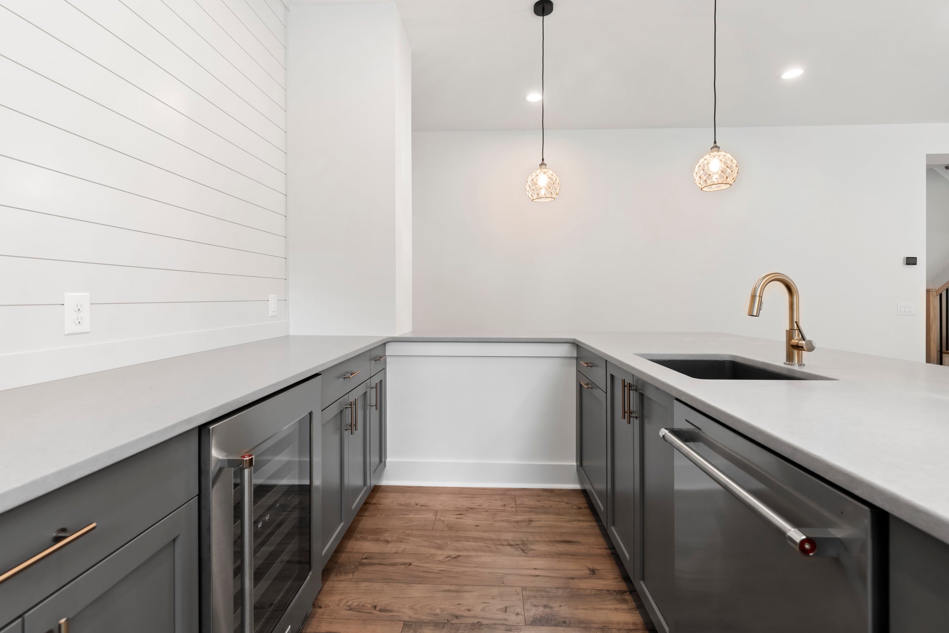 Kitchen with gray cabinets, white countertops, wine fridge, gold faucet, and two pendant lights over hardwood floors