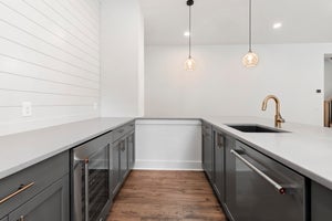 Kitchen with gray cabinets, white countertops, wine fridge, gold faucet, and two pendant lights over hardwood floors