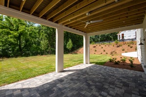 Covered patio with stone pavers, ceiling fan, and open backyard with fresh landscaping and fenced yard.