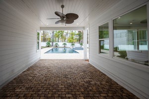 Covered patio with brick pavers and ceiling fan overlooking a backyard pool with palm trees