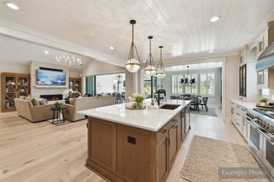 Open-concept kitchen with large wood island, white countertops, and pendant lights, flowing into living and dining areas with shiplap ceiling.