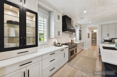 White kitchen with glass-front cabinets, black range hood, stainless gas stove, and light hardwood floors
