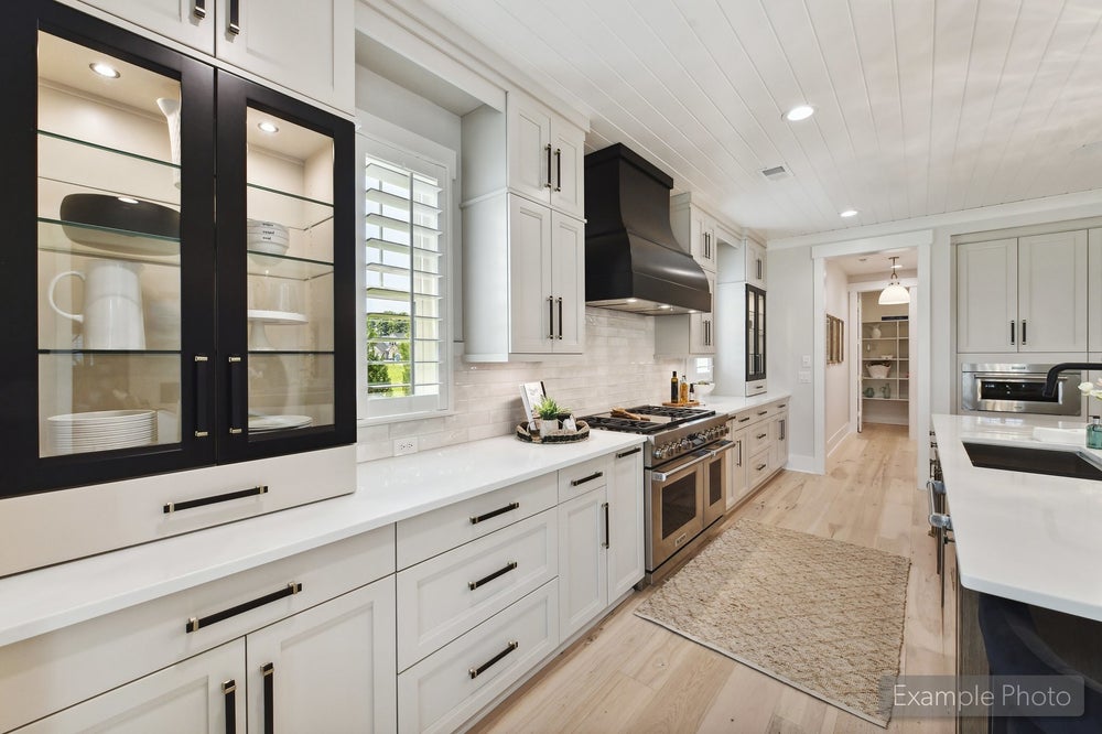 White kitchen with glass-front cabinets, black range hood, stainless gas stove, and light hardwood floors