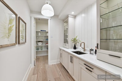 Butler's pantry with white cabinets, undermount sink, glass shelving, and walk-in pantry access on light hardwood floors