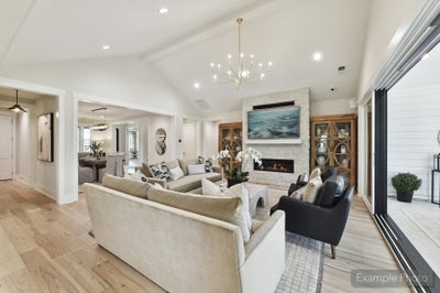 Open living room with vaulted ceiling, stone fireplace, chandelier, and hardwood floors open to dining area