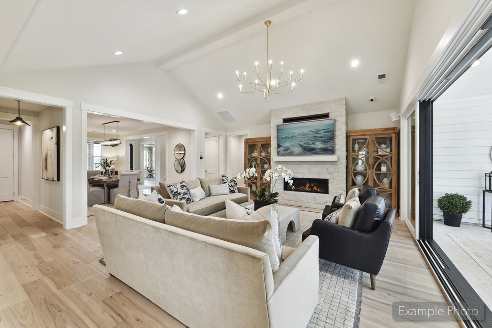 Open living room with vaulted ceiling, stone fireplace, chandelier, and hardwood floors open to dining area