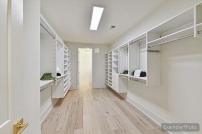 Spacious walk-in closet with white built-in shelving, hanging rods, and light hardwood floors