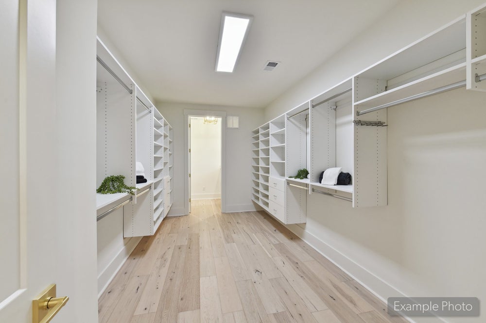 Spacious walk-in closet with white built-in shelving, hanging rods, and light hardwood floors