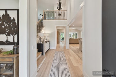 Two-story entryway with light hardwood floors, staircase with iron railing, and open view to living room