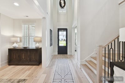 Bright foyer with two-story ceiling, black front door, hardwood floors, and staircase with iron balusters